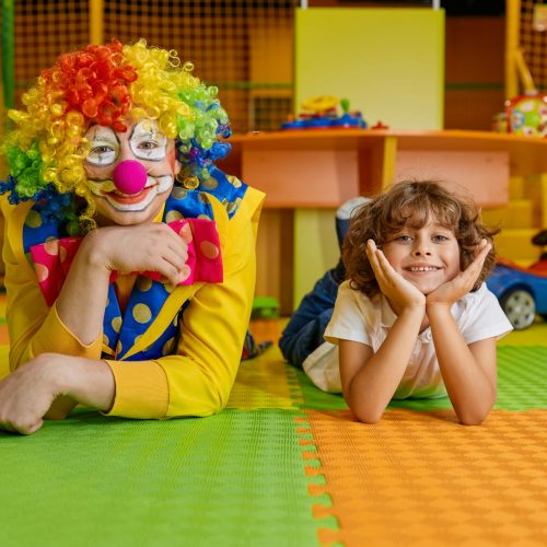 Portrait of happy smiling clown and little boy child lying on floor